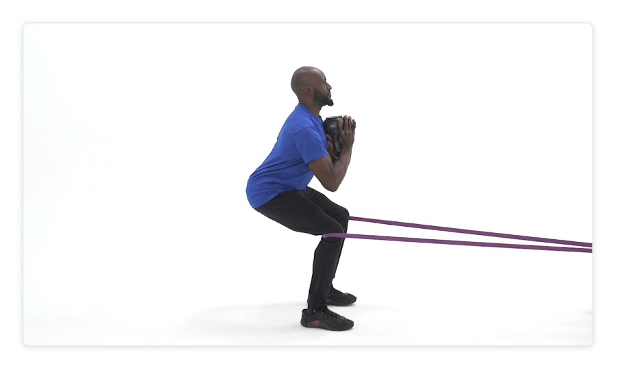 An image of a person in a blue shirt and black pants on a white background, using a resistance band and doing a squat.
